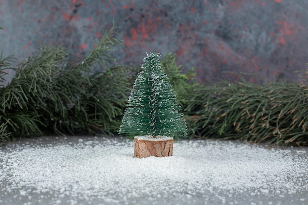 Minuscola statuina di albero di natale accanto a un ramo di albero sempreverde su una superficie di marmo