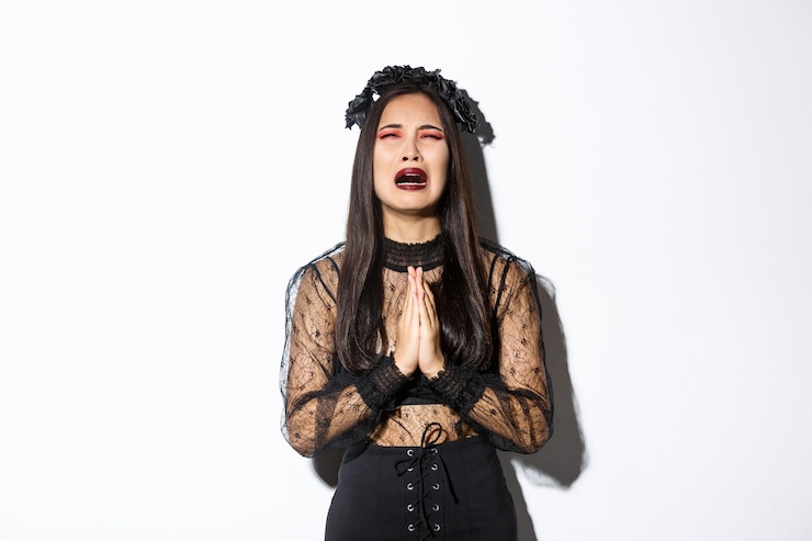Foto gratuito misera giovane donna asiatica nei guai implorando dio, piangendo e implorando aiuto, indossando abiti gotici e ghirlande di halloween, supplicando su sfondo bianco.