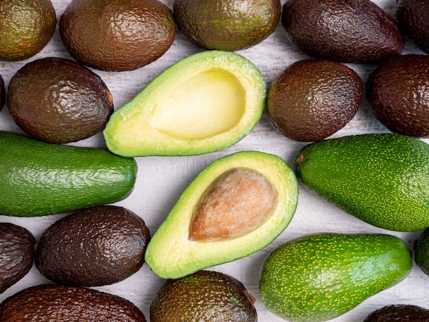 Mix di avocado strappati e verdi su tavola di legno bianca.