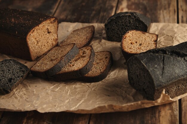 Mix di due rustici pani fatti in casa, carbone nero e segale marrone con fichi, affettato su carta artigianale isolato su un tavolo di legno