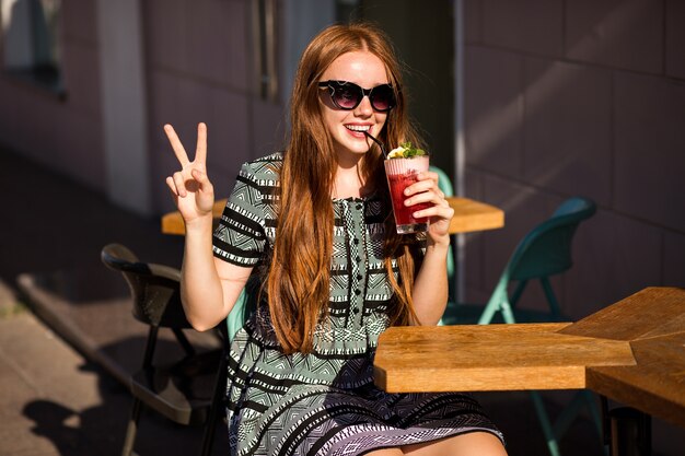 Moda giovane donna con i capelli lunghi e un sorriso incredibile, che tiene una gustosa limonata cocktail estivo dolce
