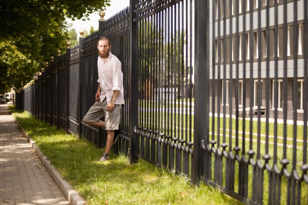 Moda hipster barbuto in posa accanto a una recinzione. Stile e diversità