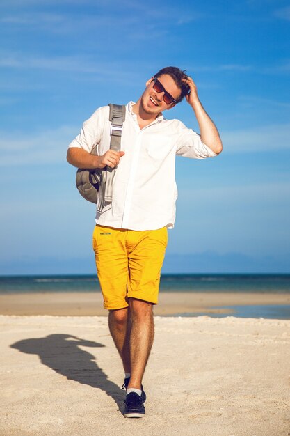 Moda ritratto all'aperto dell'uomo bello in abito casual alla moda luminoso che cammina alla spiaggia tropicale