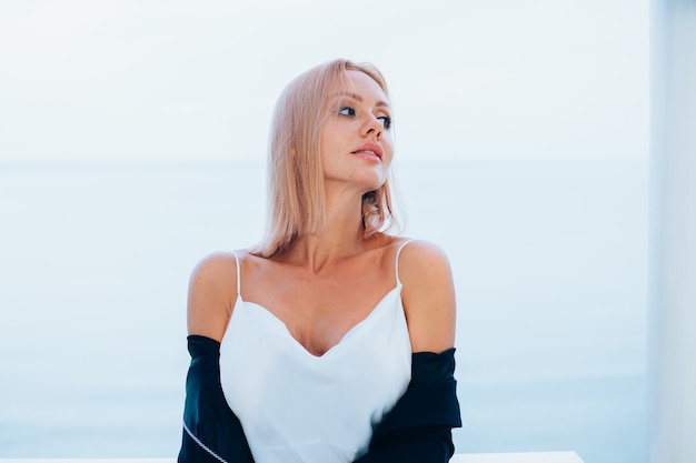 Moda ritratto di donna caucasica alla moda in blazer nero abito lungo di seta in luogo di lusso con vista sul mare