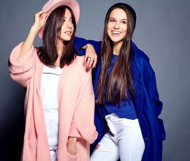 moda ritratto di due modelli sorridenti delle donne del brunette in cappotto casuale dei pantaloni a vita bassa di estate che propone sul gray