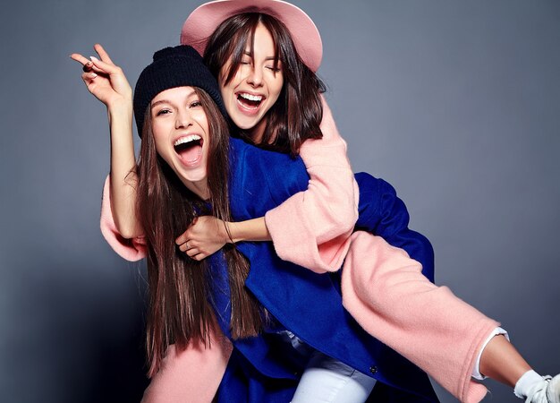 moda ritratto di due modelli sorridenti delle donne del brunette nella posa casuale del cappotto dei pantaloni a vita bassa di estate. Ragazze che si tengono sulla schiena