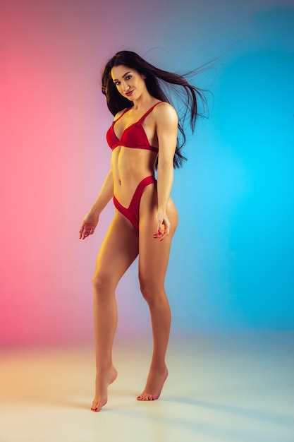 Moda ritratto di giovane donna sportiva e in forma in elegante costume da bagno di lusso rosso su parete sfumata corpo perfetto pronto per l'estate