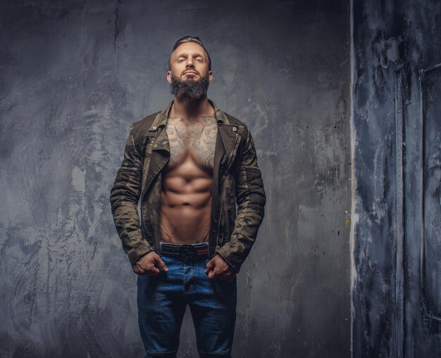 Moda uomo tatuato con barba in blue jeans e giacca sul corpo nudo.