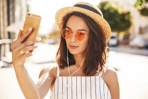 modella bruna in abiti estivi in posa sulla strada utilizzando il telefono cellulare