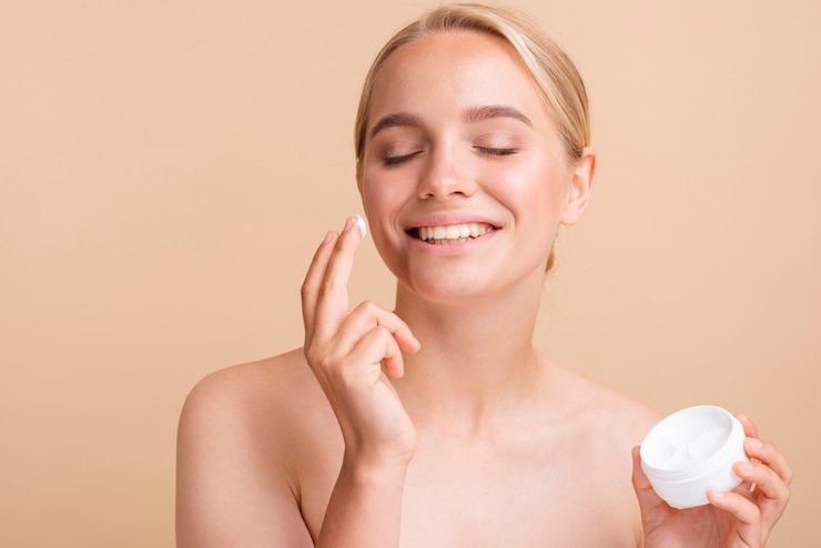 Foto gratuito modello biondo del primo piano che usando crema per il viso