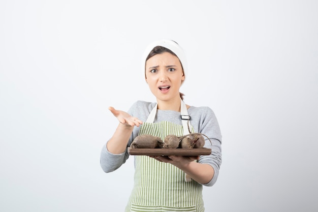 modello di donna abbastanza giovane in grembiule che tiene una tavola di legno con barbabietole.