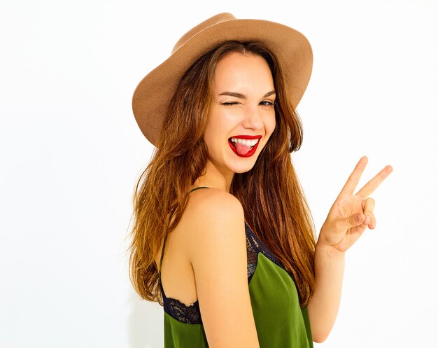 Modello di giovane donna alla moda in abiti casual estate verde e cappello marrone con labbra rosse. Strizza l'occhio e mostra la sua lingua
