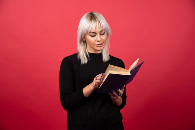 Modello di giovane donna che legge un libro su uno sfondo rosso. Foto di alta qualità