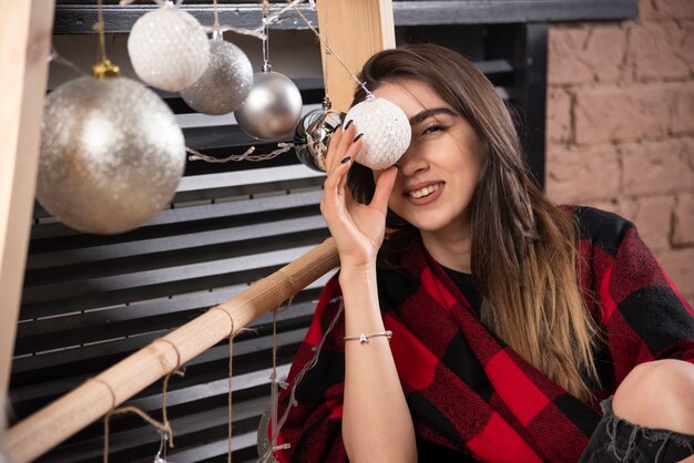 Modello di giovane donna in posa con plaid a scacchi vicino alle palle di Natale.