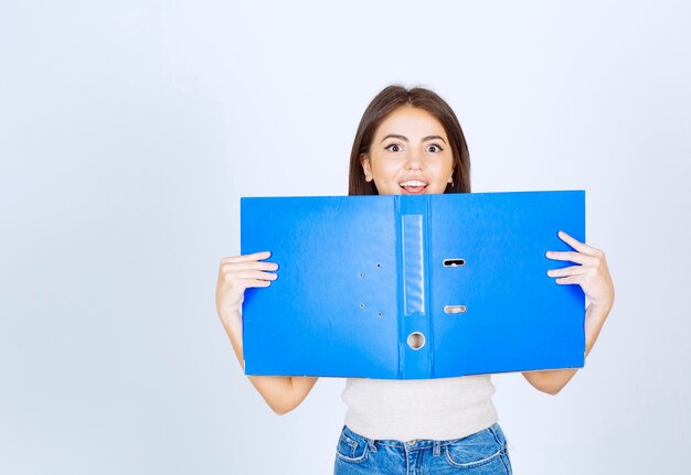 modello di giovane donna in possesso di una cartella blu sul muro bianco.