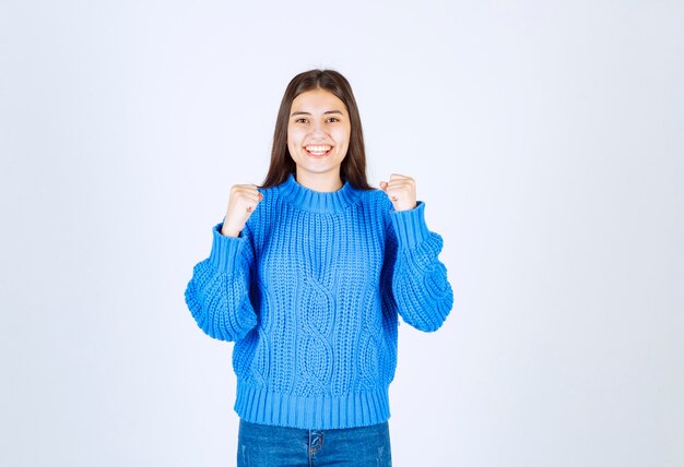 modello di giovane ragazza in maglione blu in piedi e in posa su bianco-grigio.