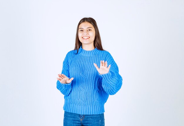 modello di giovane ragazza in maglione blu in piedi e in posa su bianco-grigio.