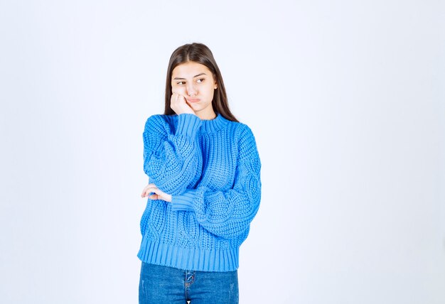 modello di giovane ragazza in maglione blu in piedi e in posa su bianco-grigio.