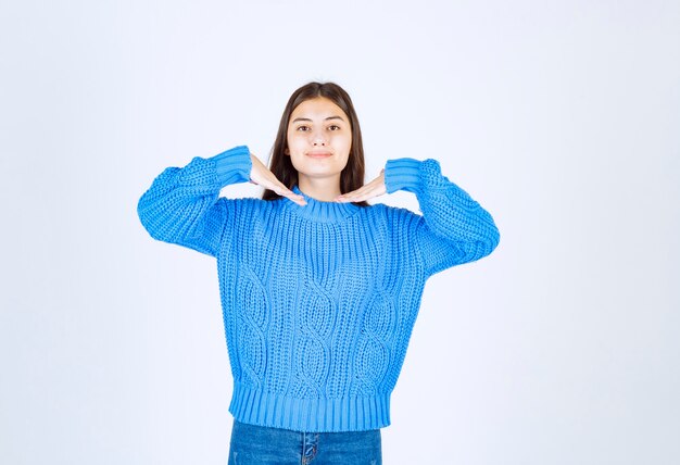 modello di giovane ragazza in maglione blu in piedi e in posa su bianco-grigio.