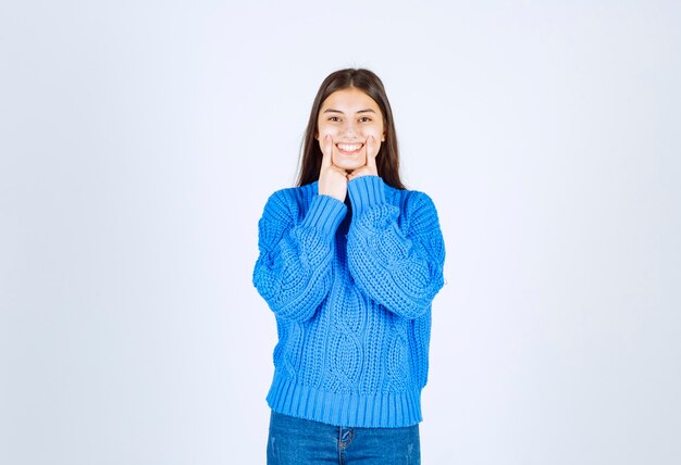 modello di giovane ragazza in maglione blu in piedi e in posa su bianco-grigio.