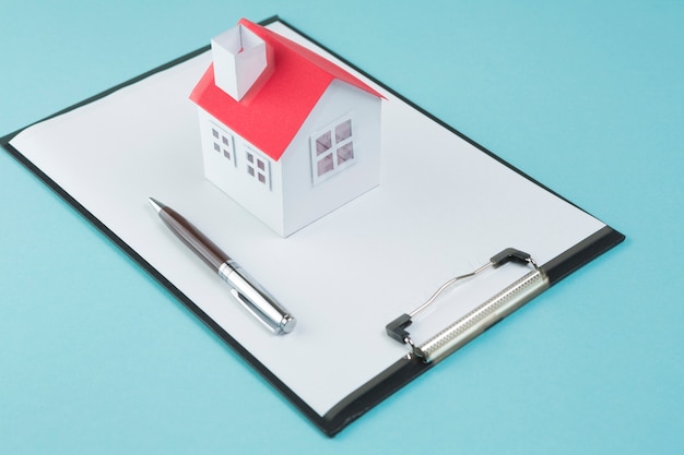 Modello di piccola casa e penna su appunti vuoto su sfondo blu