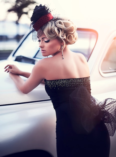 modello di ragazza bionda bella moda sexy con trucco luminoso e acconciatura riccia in stile retrò, seduto nella vecchia auto