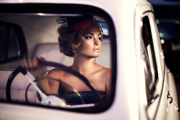 modello di ragazza bionda bella moda sexy con trucco luminoso e acconciatura riccia in stile retrò, seduto nella vecchia auto
