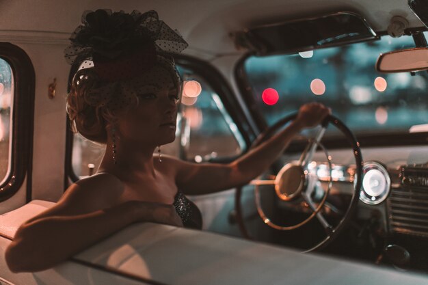 modello di ragazza bionda bella moda sexy con trucco luminoso e acconciatura riccia in stile retrò, seduto nella vecchia auto
