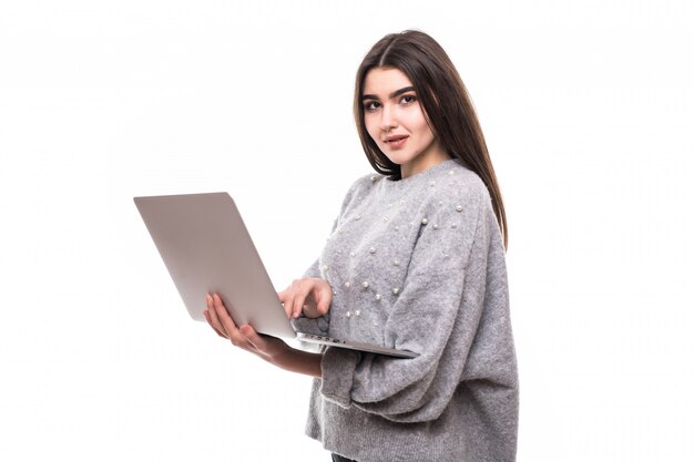 Modello di ragazza bruna in maglione grigio si siede sul pavimento e lavora studie sul suo laptop