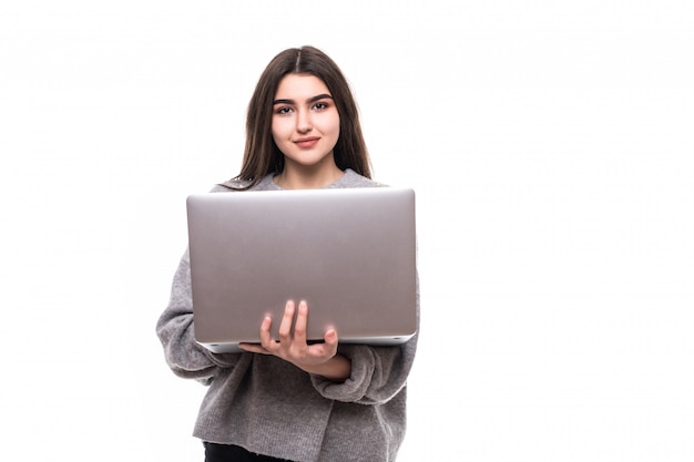Modello di ragazza bruna in maglione grigio stand e studio di lavoro sul suo laptop