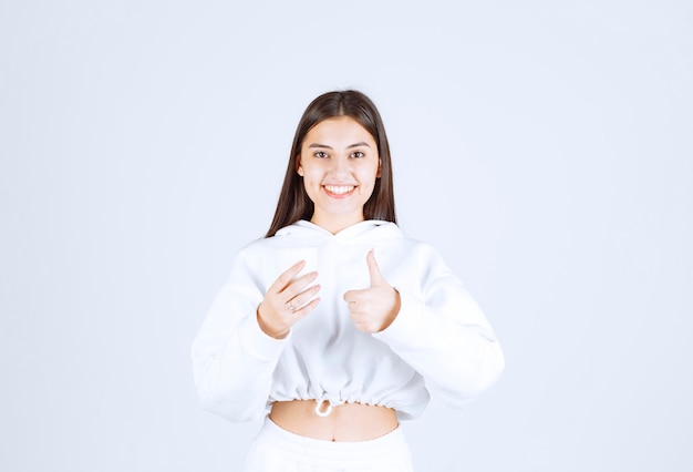 modello di ragazza carina con un bicchiere di plastica che mostra un pollice in su.