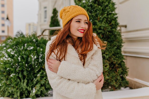 Modello femminile allegro in camice bianco che posa in una giornata fredda Scatto all'aperto di una bella signora di zenzero in piedi sulla strada