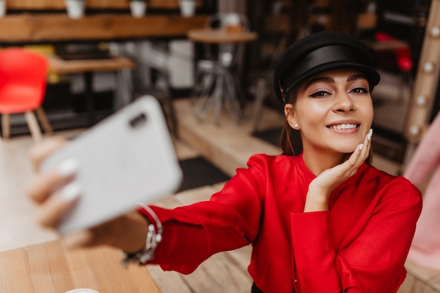 Modello femminile di 22 anni con un trucco nudo, vestito con un vestito rosso delicato, che completa il braccialetto d'argento, fa un selfie fantastico