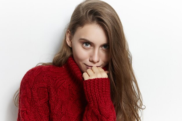 Modello femminile europeo giovane affascinante affascinante con capelli sciolti disordinati in posa isolato in maglione dolcevita accogliente, con espressione facciale civettuola Bella ragazza che indossa un elegante pullover marsala cozt