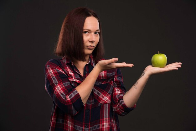 Modello femminile in abiti da collezione autunno inverno tenendo una mela verde e indicandola.