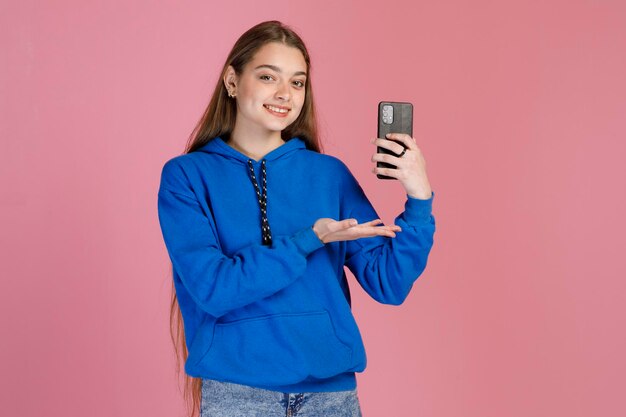 Modello femminile sorridente che dimostra il nuovo smartphone con la mano mentre guarda la fotocamera