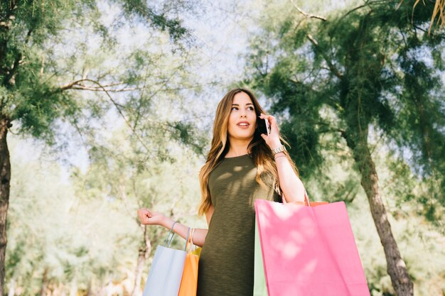 Modello femminile, telefono e borse per la spesa nel parco