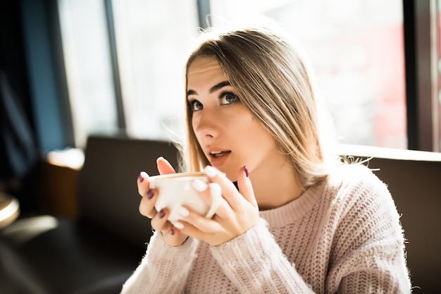 Modello grazioso in un maglione alla moda, seduto in un bar con una tazza di tè e caffè ogni giorno