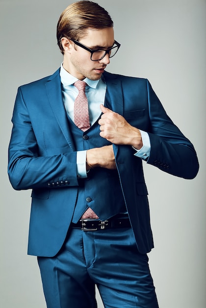 Modello maschio del giovane uomo d'affari bello elegante in vestito blu e vetri alla moda, posanti nello studio