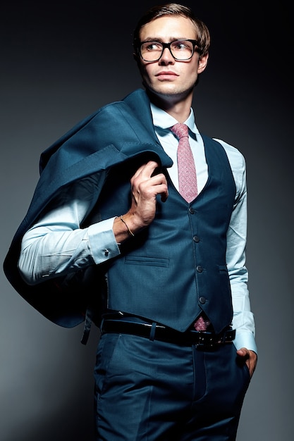 Modello maschio del giovane uomo d'affari bello elegante in vestito blu e vetri alla moda, posanti nello studio