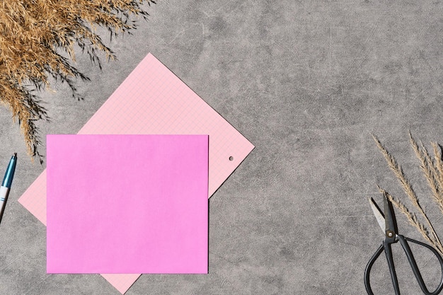 Modello vuoto per un layout con un invito o una nota in una busta viola su sfondo grigio decorato con erba secca Scheda di carta bianca nella busta artigianale vista dall'alto della busta della lettera e della penna