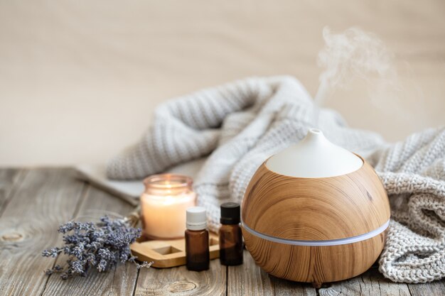 Moderno diffusore di oli aromatici su superficie in legno con elemento in maglia, candela e olio di lavanda su uno sfondo sfocato.