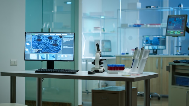 Moderno laboratorio di scienze applicate biologiche vuote con microscopi tecnologici, provette di vetro, micropipette, computer desktop e display. I PC eseguono sofisticati calcoli del DNA.