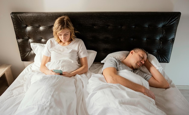 Moglie che utilizza il cellulare mentre il marito dorme