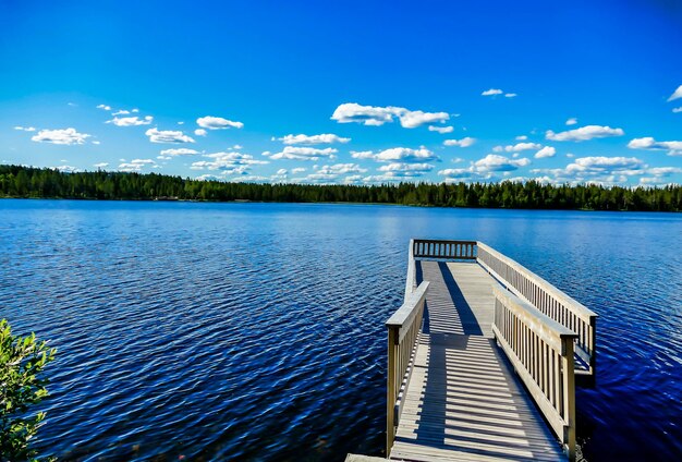 Molo in legno sul bellissimo lago con gli alberi e il cielo blu sullo sfondo in Svezia