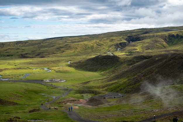 Molte persone camminano lungo uno stretto sentiero in una terra verde circondata da verdi colline