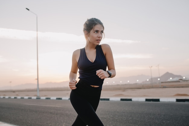 Momenti di mattina di sole felici di giovane donna stupefacente motivata laboriosa in abiti sportivi in esecuzione su strada nel paese tropicale delle Nazioni Unite di primo mattino. Formazione, allenamento, stile di vita sano