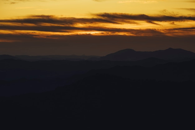 Montagna panoramica e fondo drammatico di tramonto del cielo in dorato