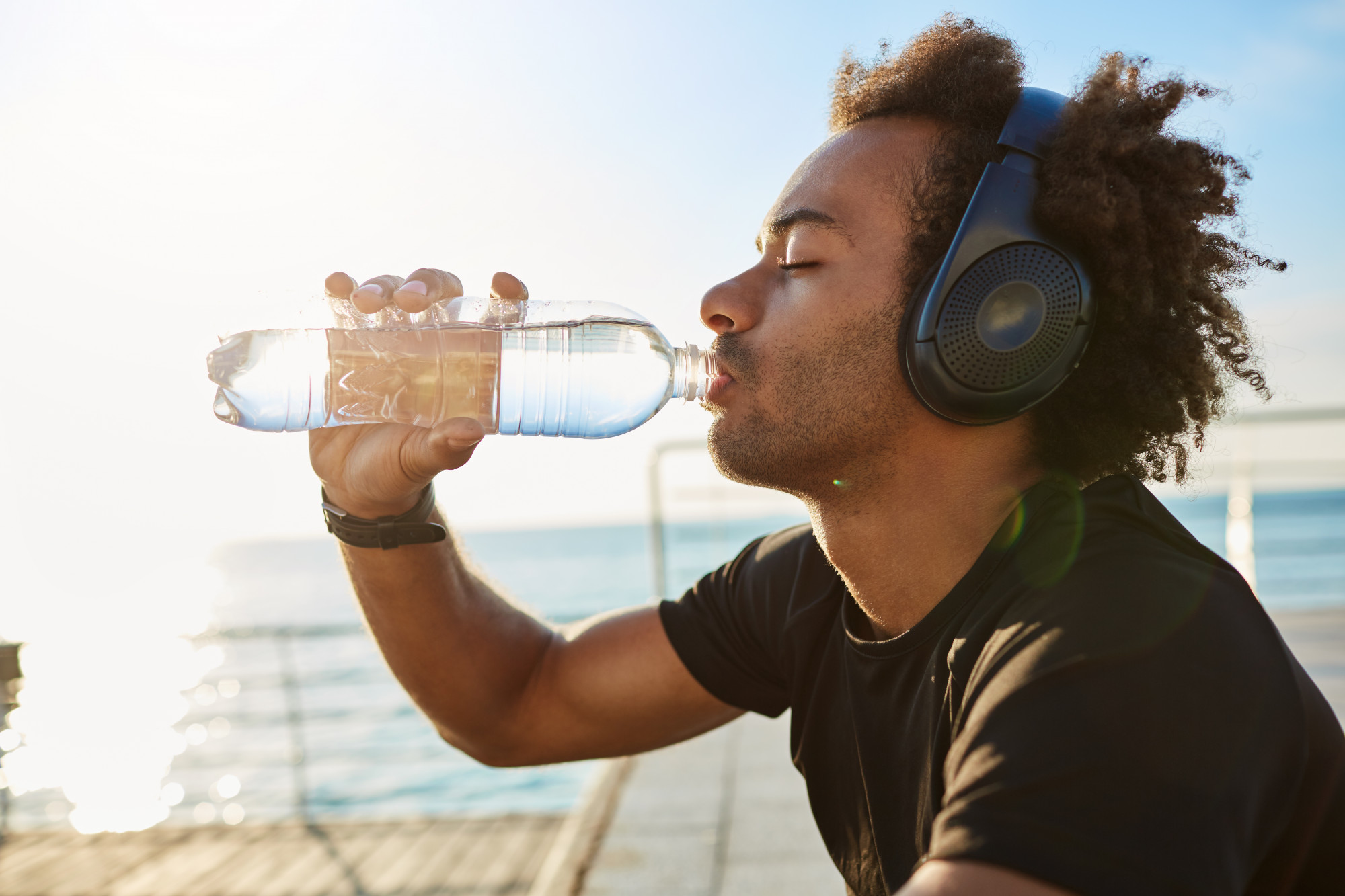 Montare l'acqua potabile dell'atleta dalla pelle scura dalla bottiglia di plastica dopo un duro allenamento cardio.