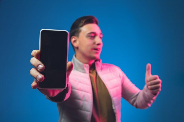 Mostrando lo schermo del telefono vuoto Ritratto di uomo caucasico sulla parete blu in luce al neon rosa.